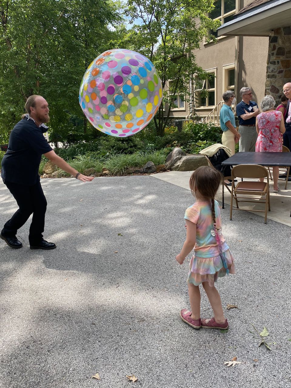 A middle-aged white man playing with a small white girl viewed from the back, with a rainbow-themed beach ball