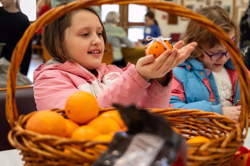 A girl in a pink jacket holds an orange.